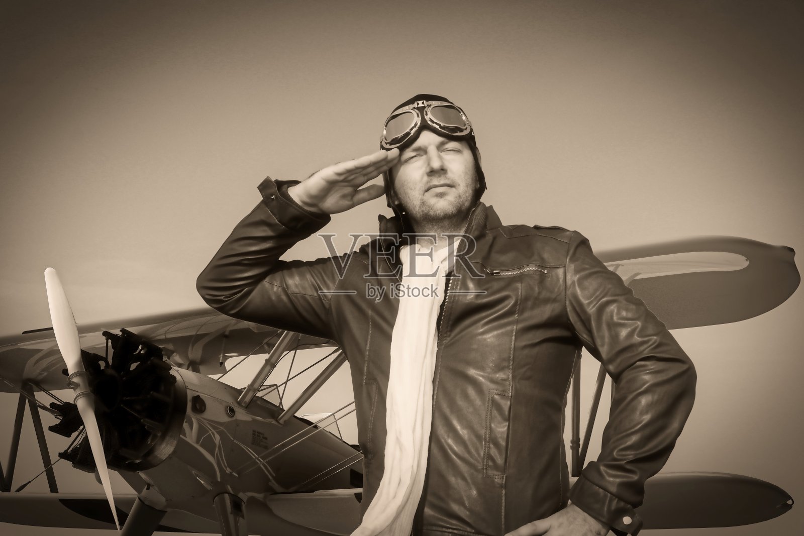 肖像的一个复古飞行员与皮革帽,围巾和飞行员眼镜在一个历史性的飞机双翼飞机前-肖像的一个人在历史性的飞行员服装-复古的老图片风格照片摄影图片