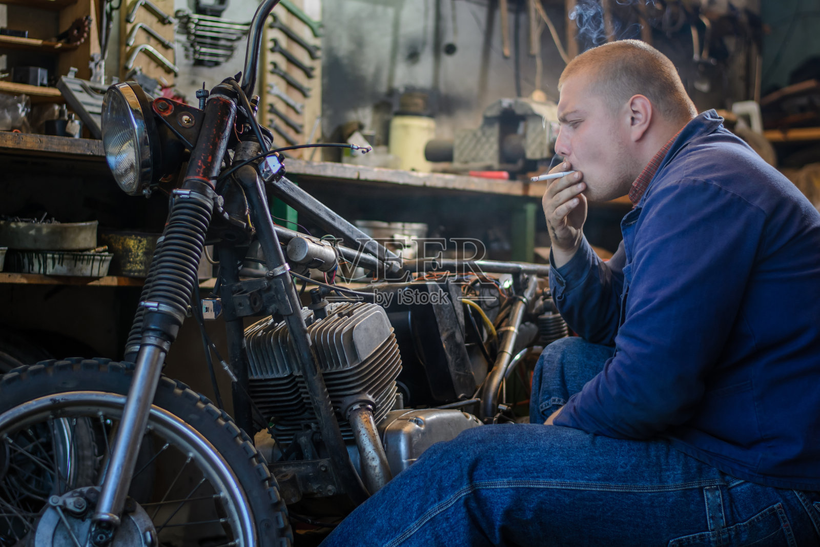 一名男子在车间修理旧摩托车时抽烟照片摄影图片