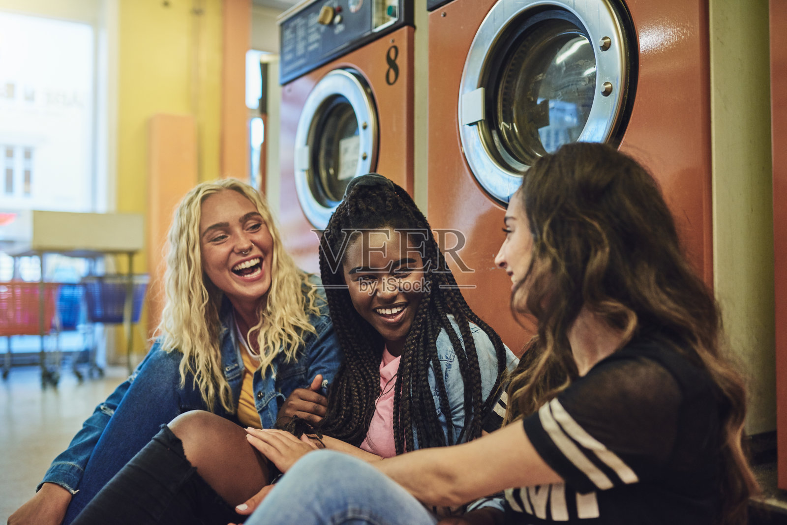 不同的年轻女友坐在洗衣店的地板上聊天照片摄影图片