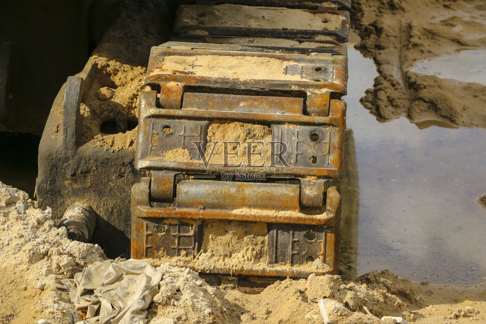 湿沙中的旧铁毛虫。生锈的钢轮和履带的大型推土机,坦克,挖掘机,在潮湿的沙子和水坑。照片摄影图片