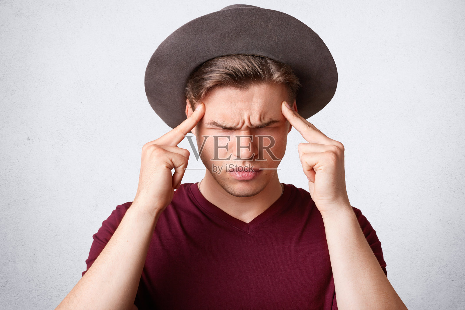 工作室拍摄的阴沉的白人男性皱眉的脸,保持食指在太阳穴,有不满的表情,在白色的背景下摆姿势。人,面部表情和消极观念。照片摄影图片