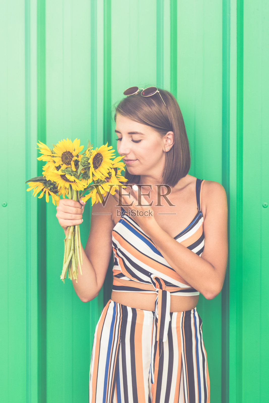 沉思的女孩与向日葵孤立在颜色的墙壁。照片摄影图片