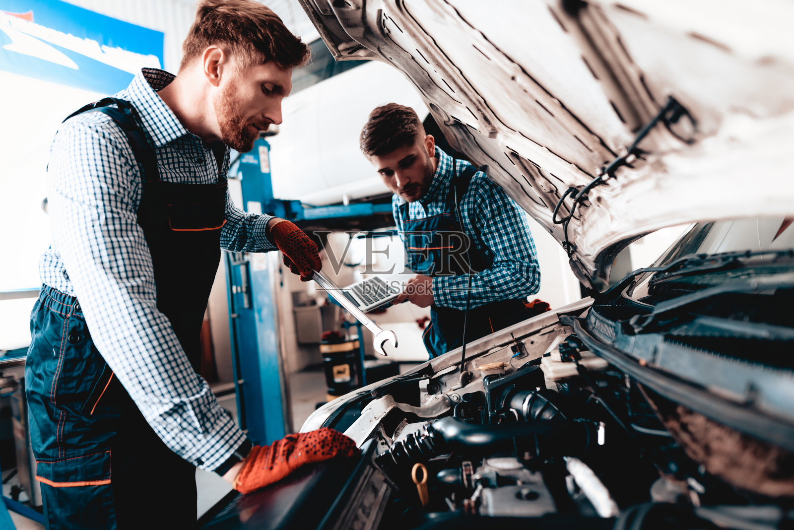 年轻的汽车机修工用扳手修理汽车。照片摄影图片