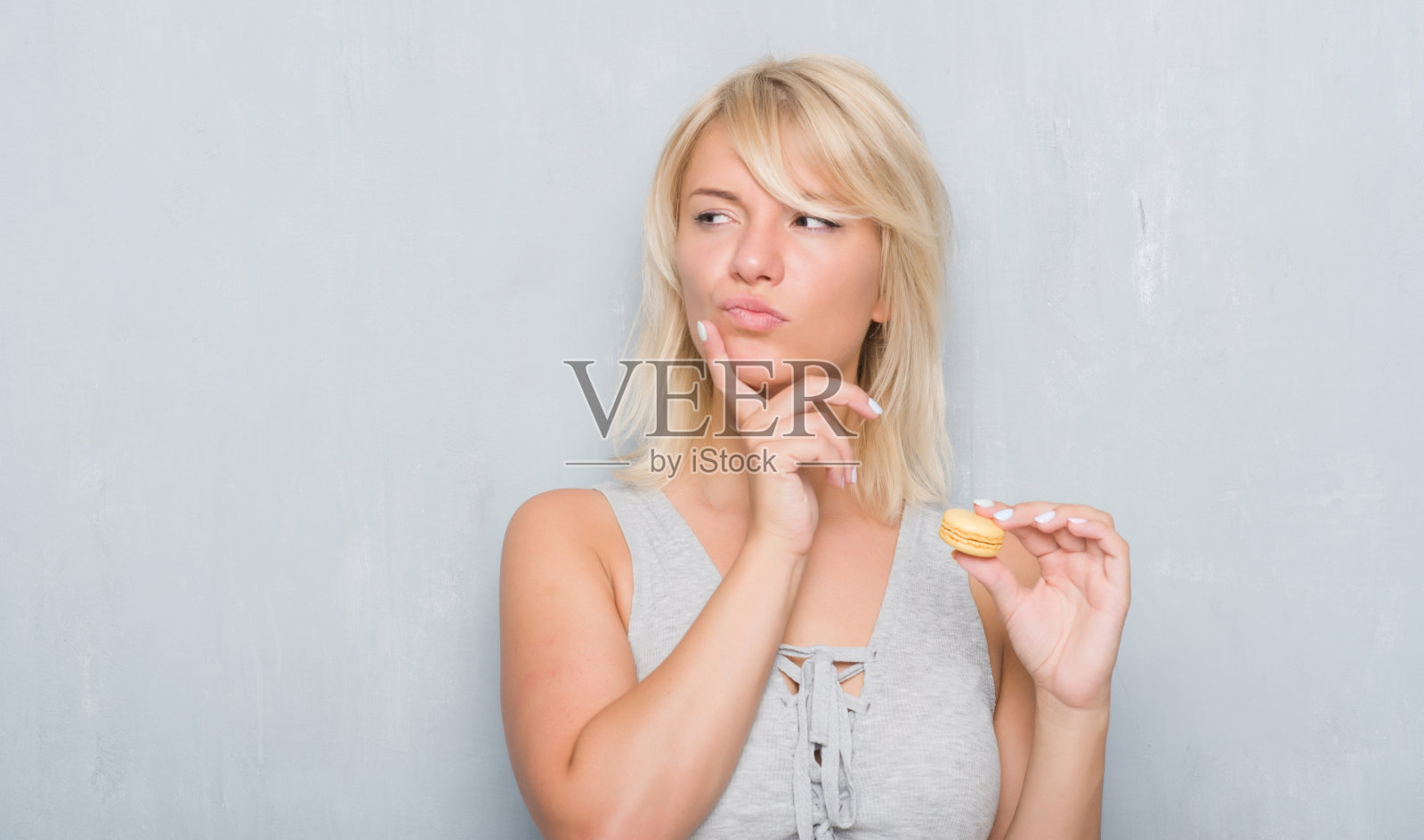 成年白种人女人过着垃圾灰墙吃着马卡龙严肃的脸上思考着问题,非常困惑的想法照片摄影图片