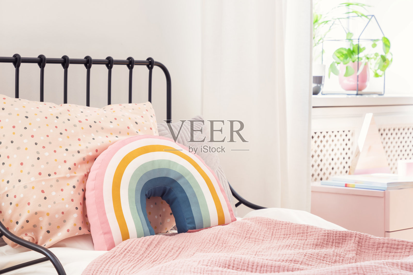 彩虹枕头和粉红色床单在女孩的床上明亮的卧室内部与植物。真实的照片照片摄影图片