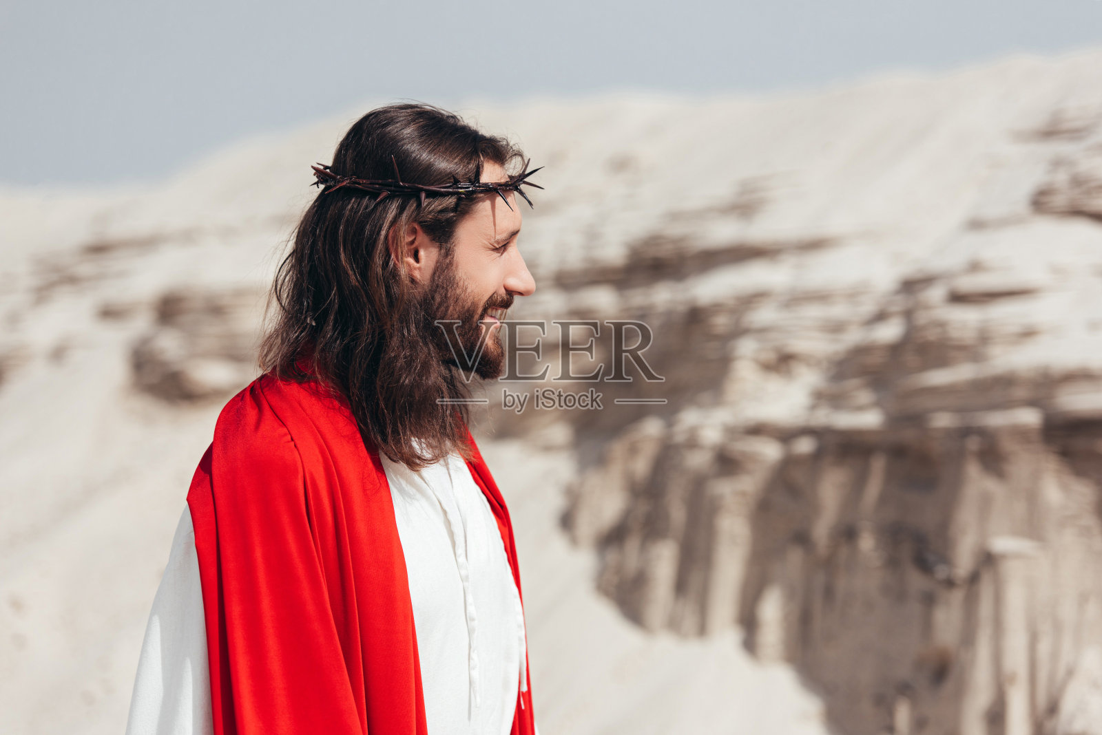 微笑的耶稣穿着袍子,红腰带和荆棘冠冕在沙漠中看着照片摄影图片