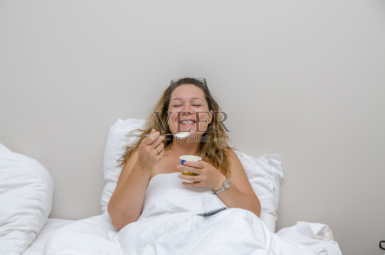 一个女人在旅馆的床上笑着,白天吃着酸奶照片摄影图片