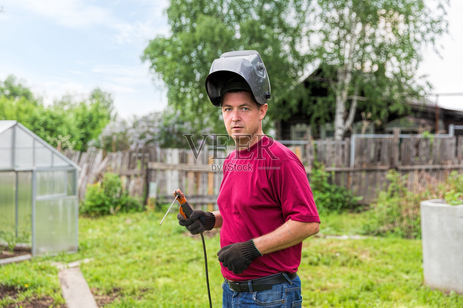 焊工戴着保护面罩,在绿草和树木的背景下工作照片摄影图片