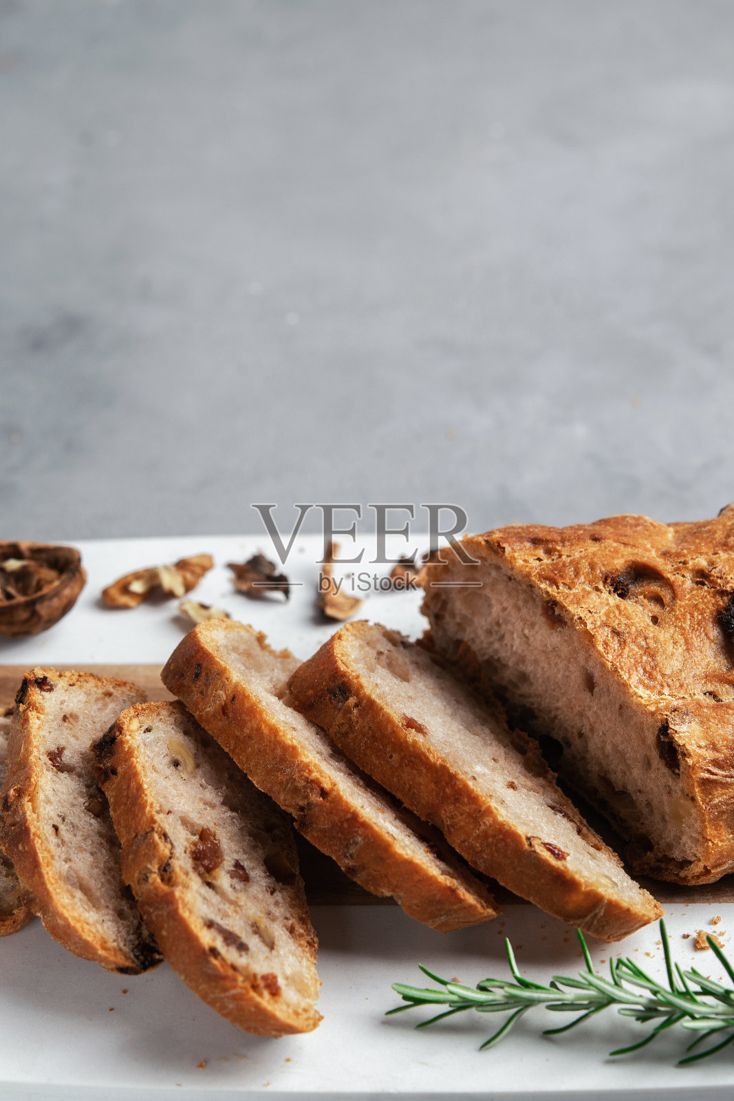 新鲜健康的切片面包,核桃和葡萄干,切板上灰色的石头背景。副本的空间。垂直的。有选择性的重点。照片摄影图片