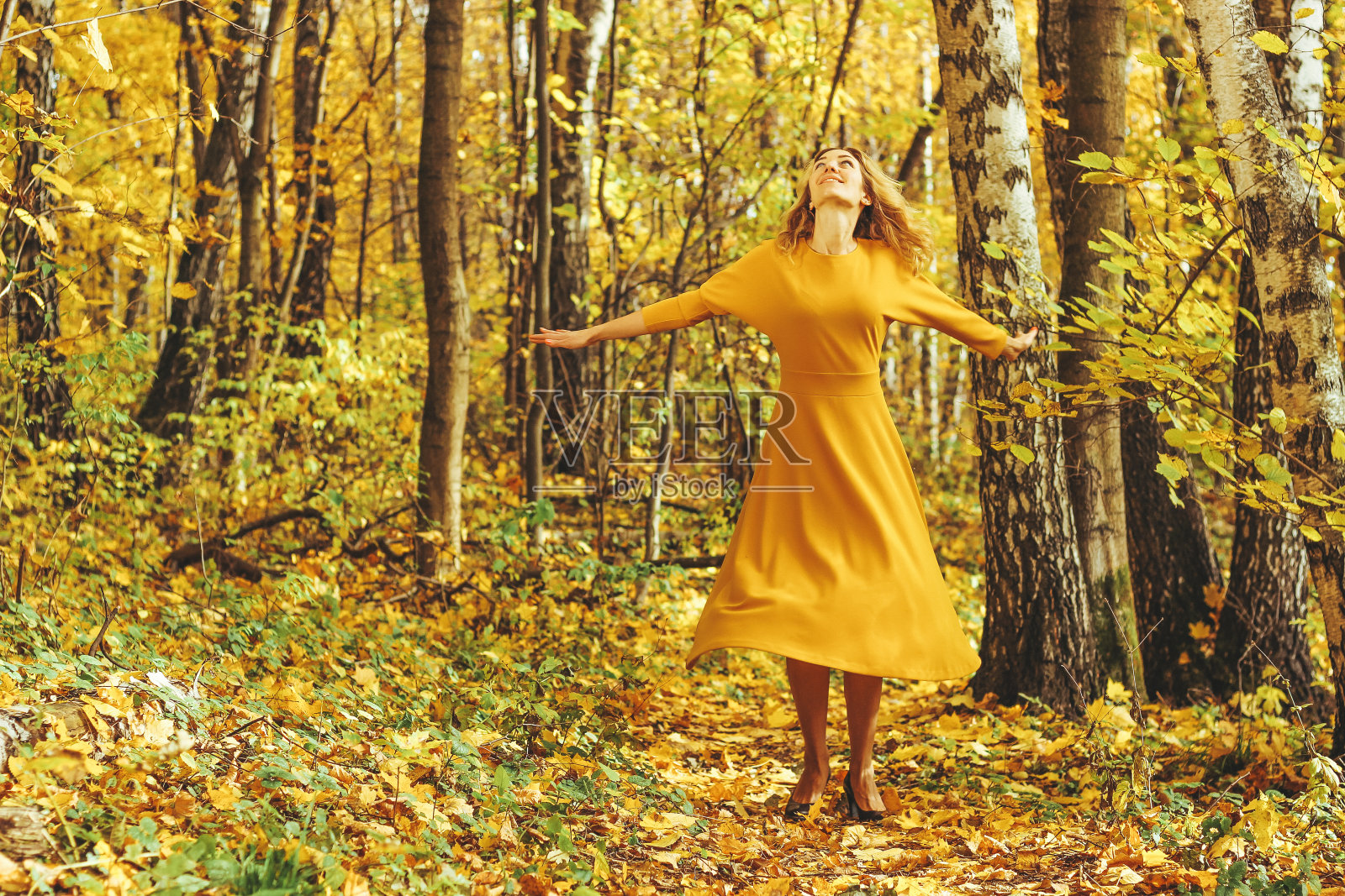 年轻美丽的女孩穿着黄色的长裙,走在落叶飘落的秋天公园里照片摄影图片