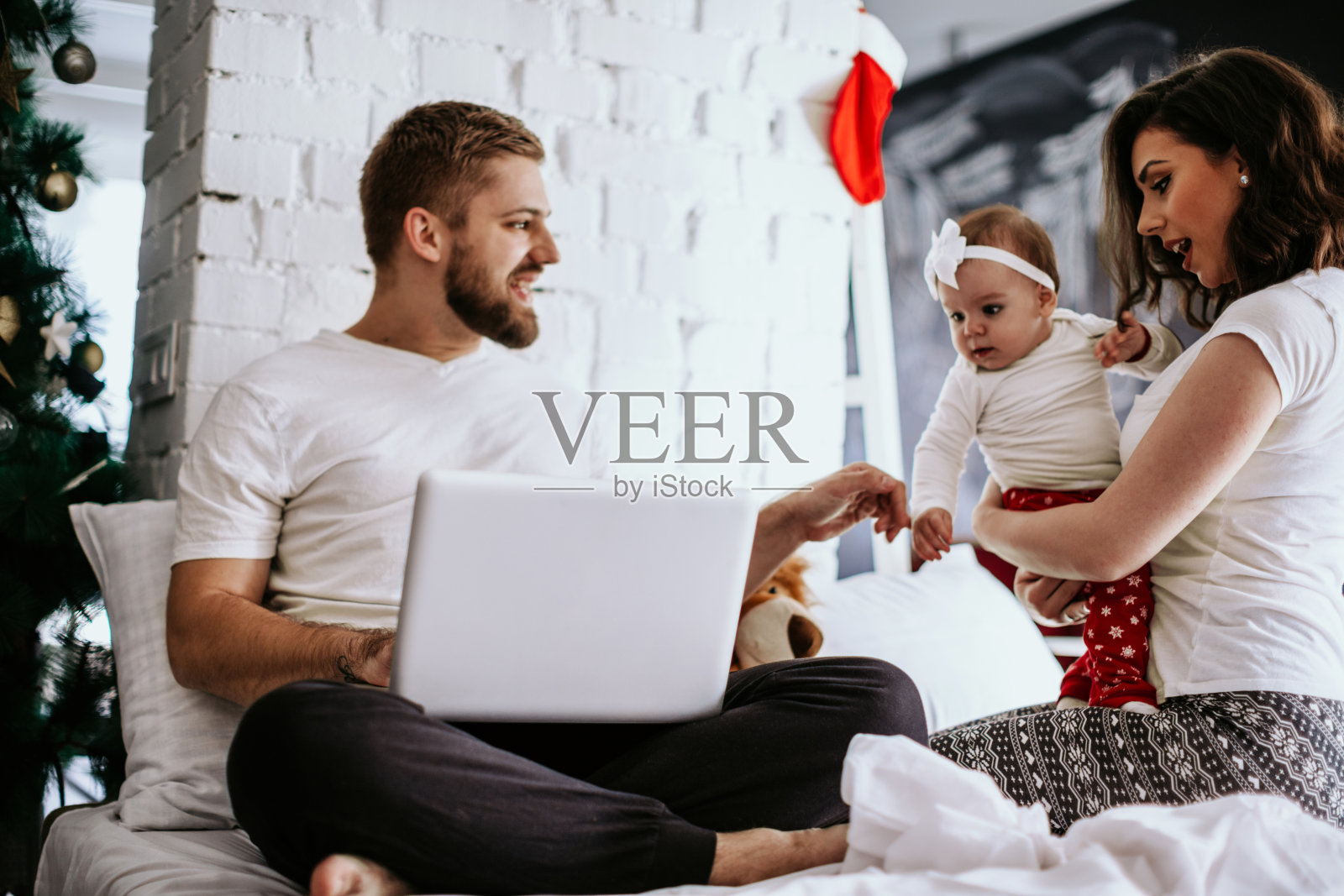 幸福的一家人在圣诞树旁的床上照片摄影图片