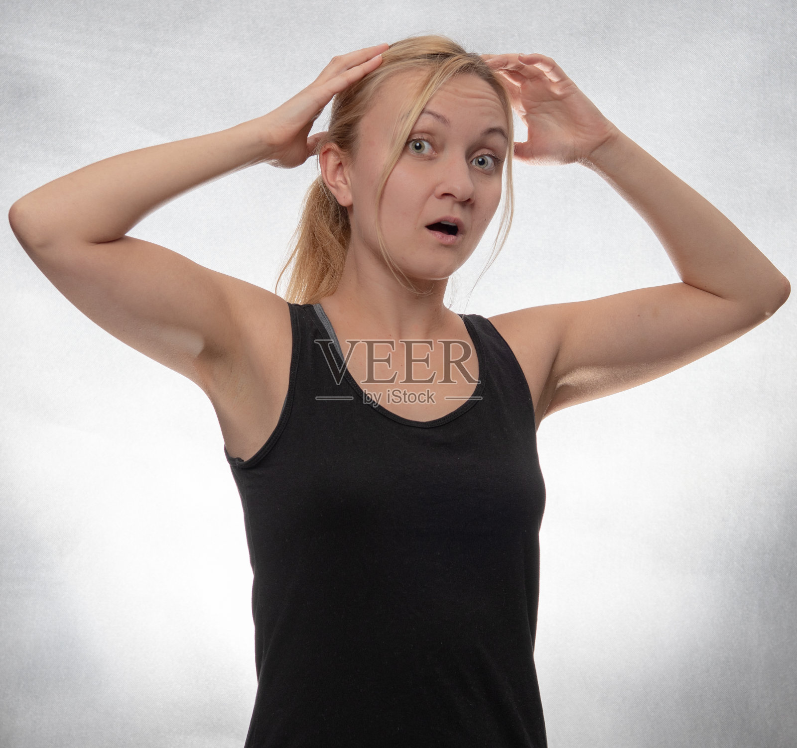 震惊的年轻女子双手放在她的头在黑色背心照片摄影图片