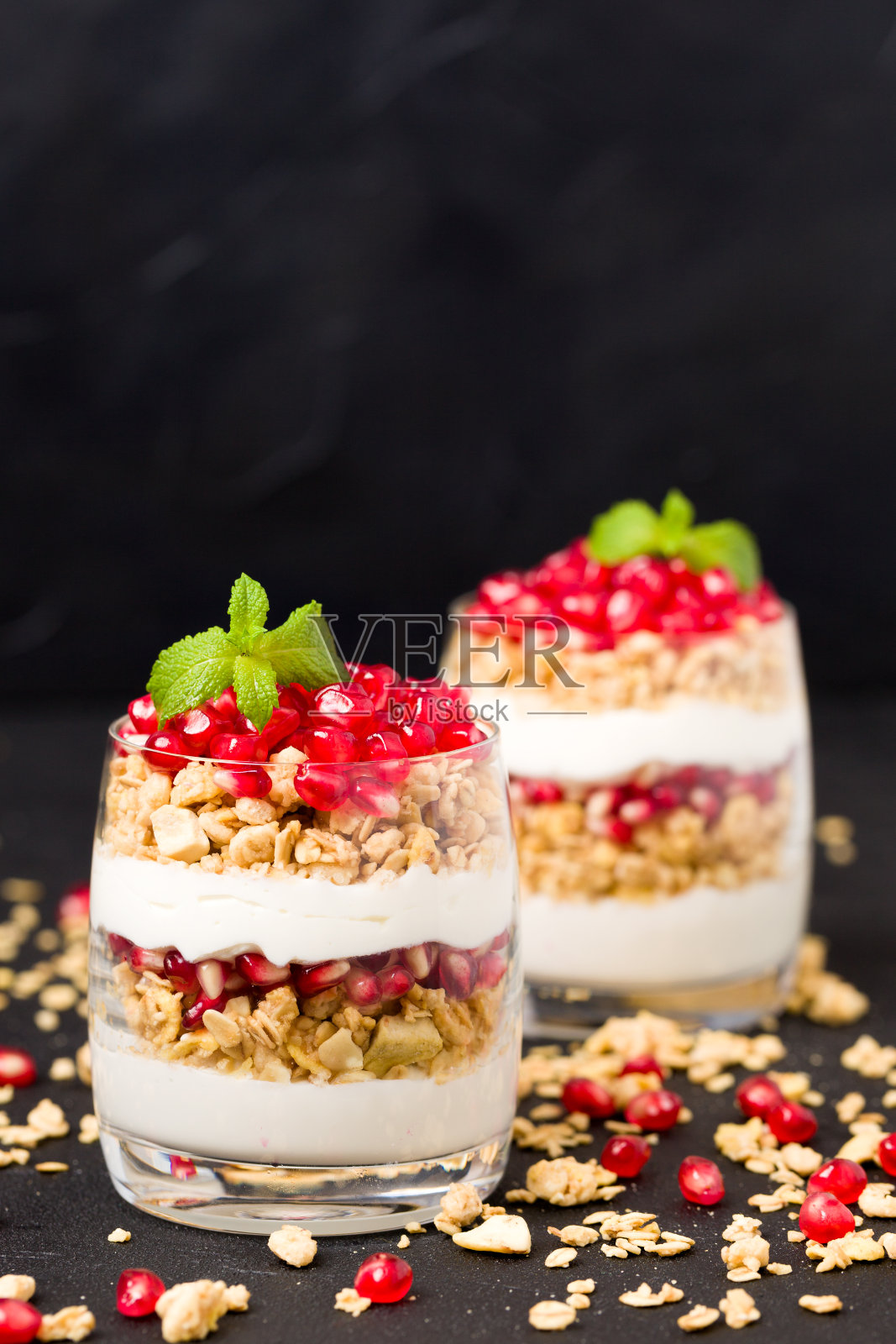 石榴冻糕——以黑色为背景,搭配格兰诺拉麦片片、酸奶和水果种子的有机甜甜品。照片摄影图片