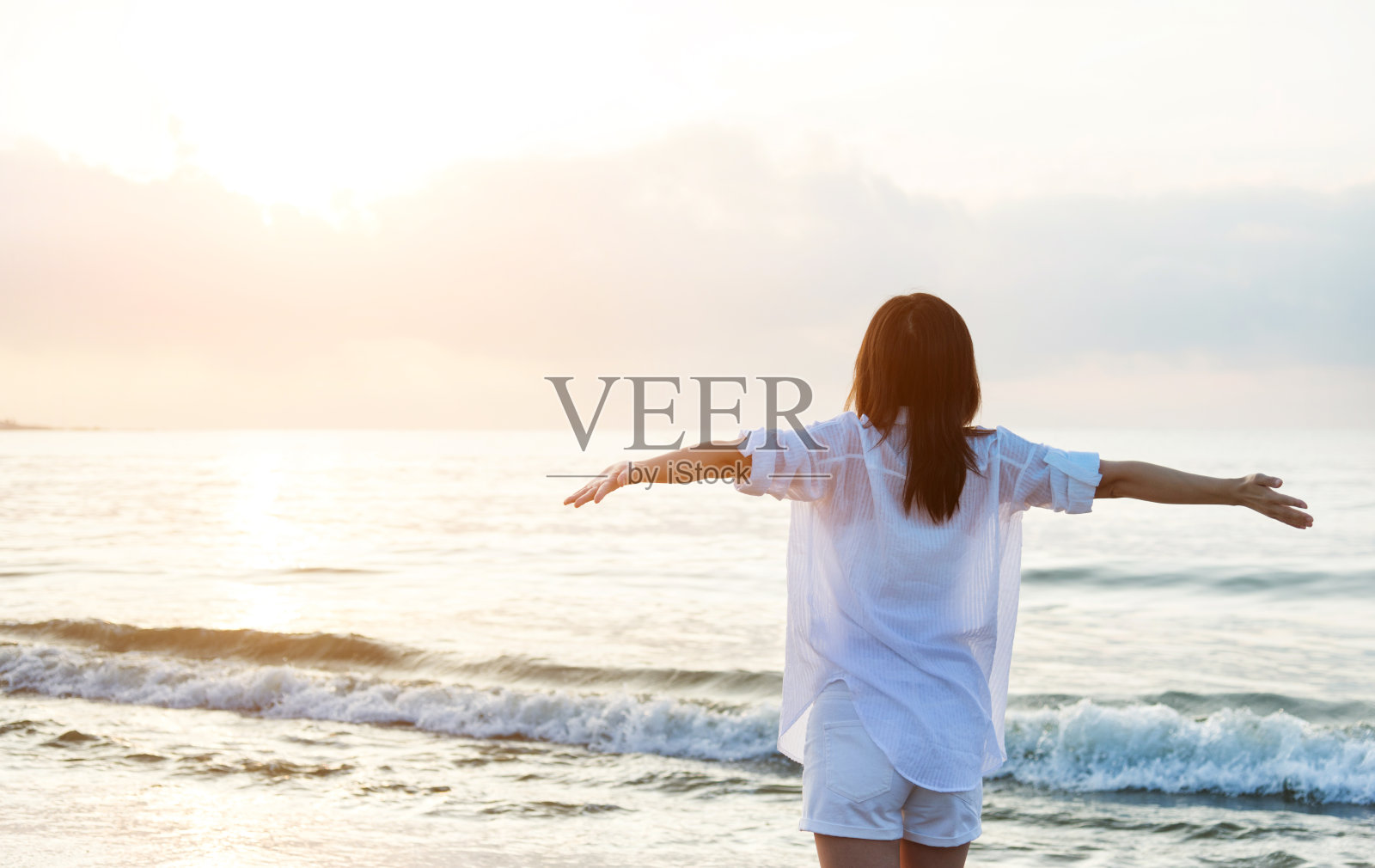 年轻女子站在沙滩上,双臂张开照片摄影图片