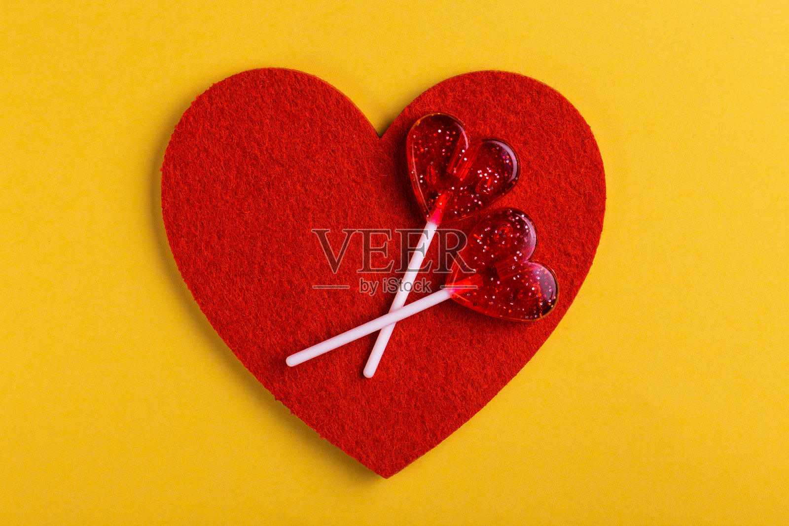 两根红色的棒棒糖和明亮的黄色背景上的心。情人节照片摄影图片