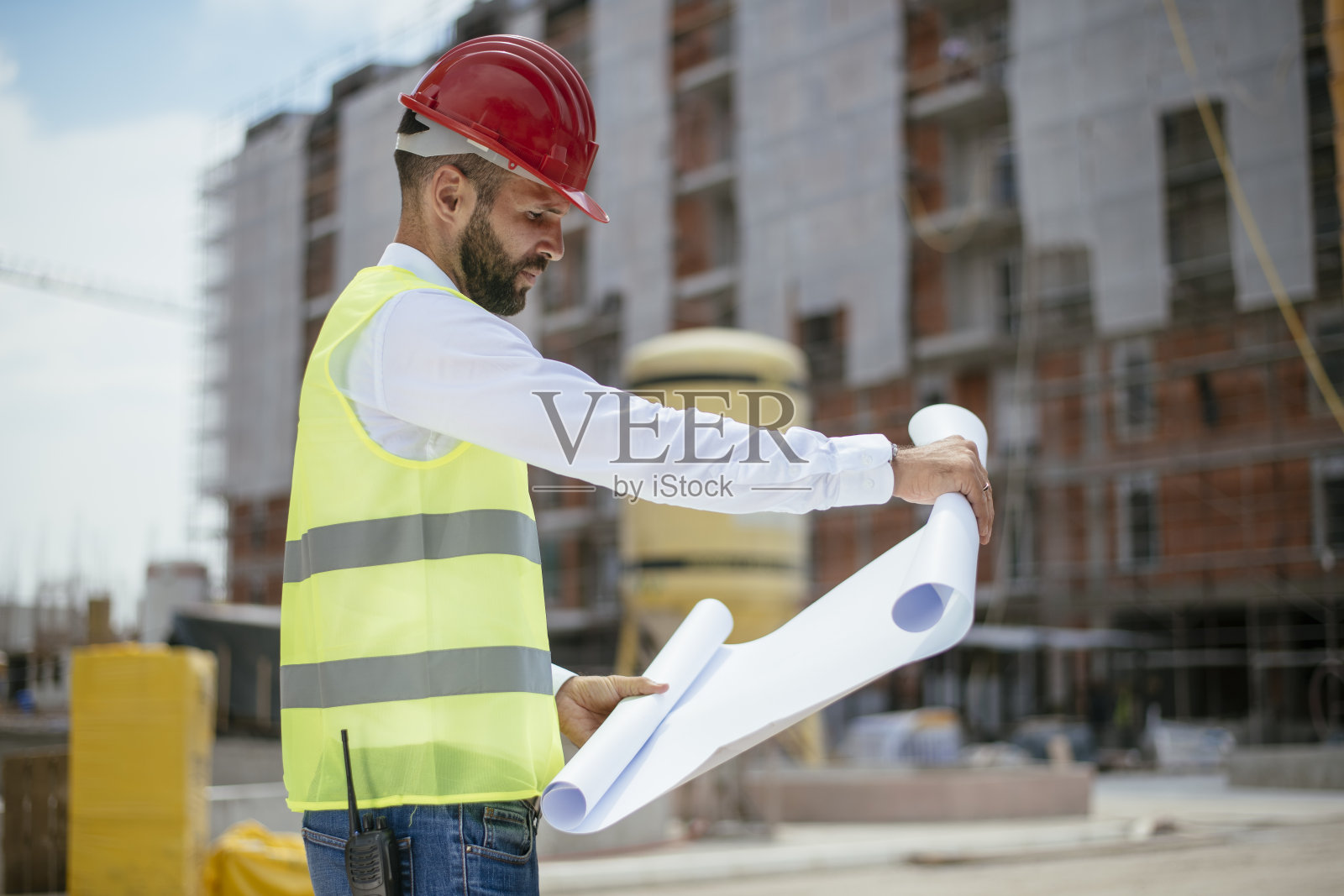 带着蓝图和戴着红色头盔的年轻建筑师照片摄影图片