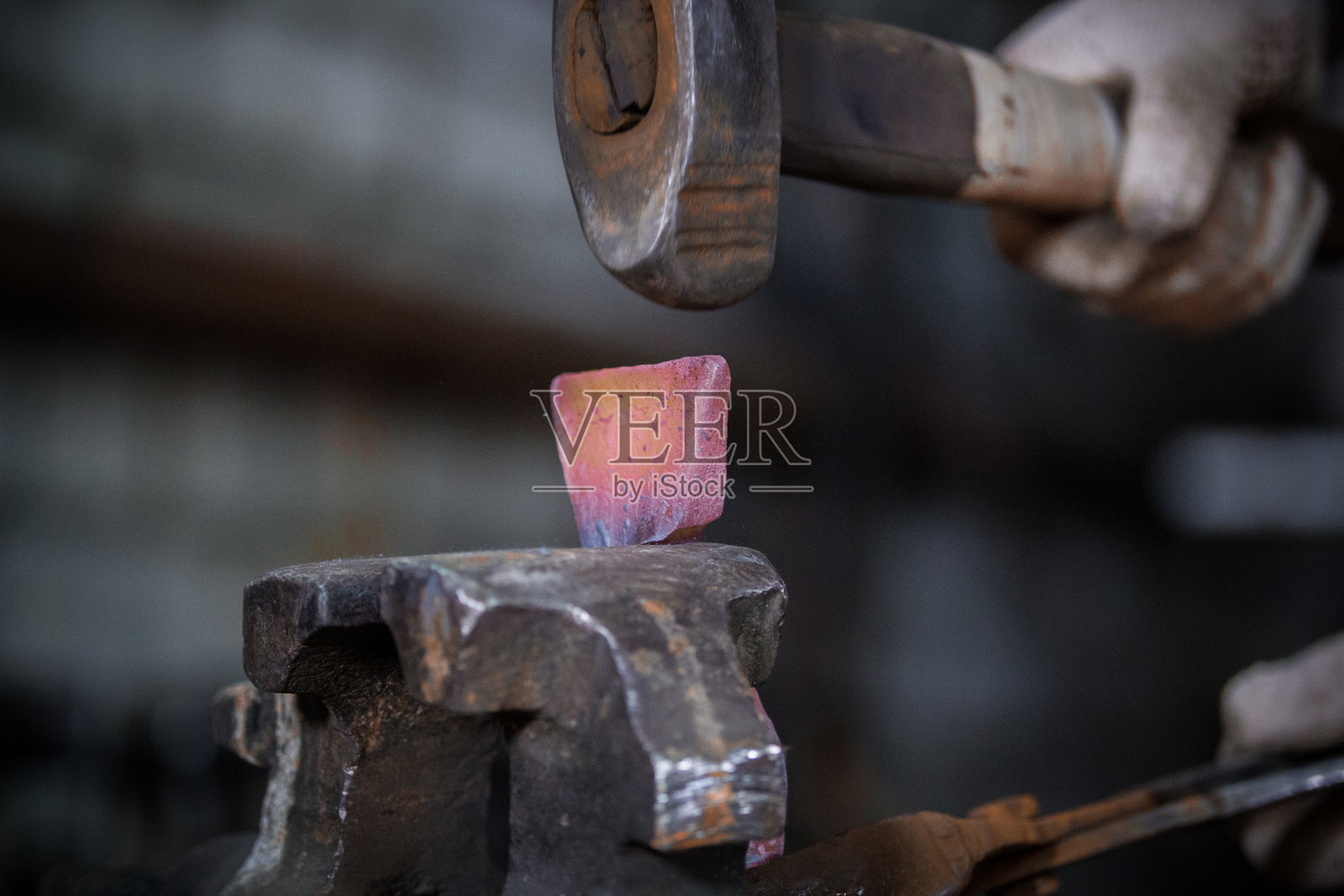 铁匠的工作空间。铁匠在锻炉的虎钳上用新铁锤加工红热的金属工件照片摄影图片