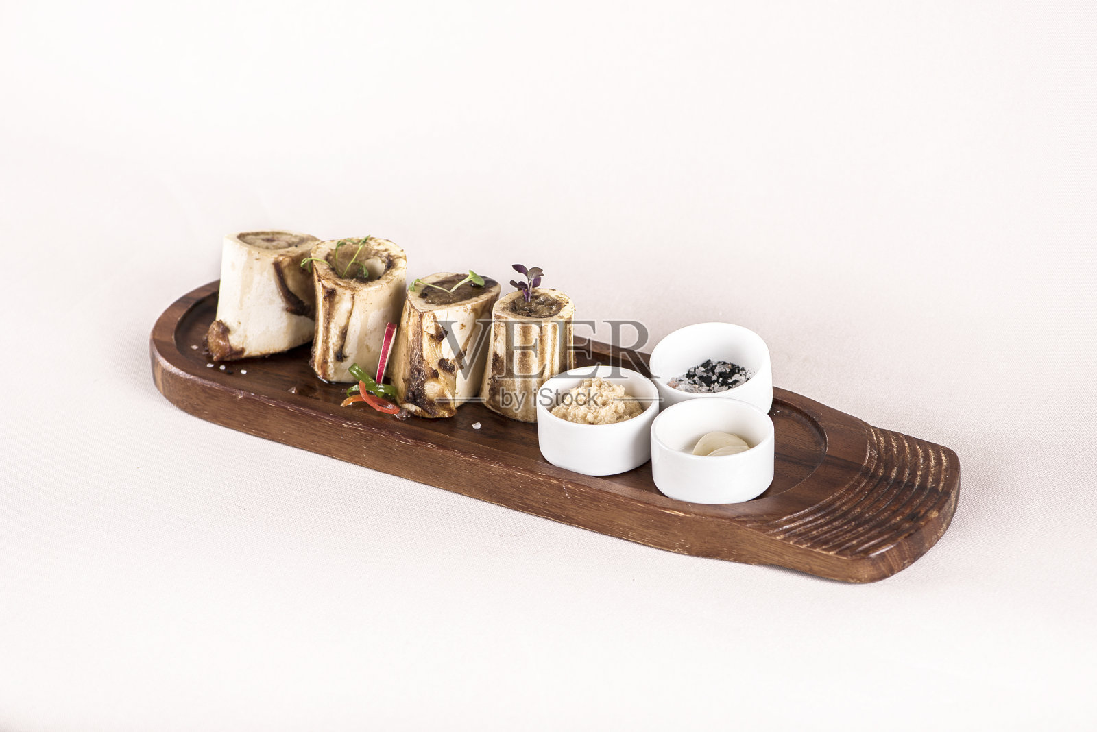 骨髓配上大蒜、辣根酱和黑色、粉色和白色的盐,放在木板上,用萝卜和新鲜的叶子装饰,浅色背景,孤立照片摄影图片