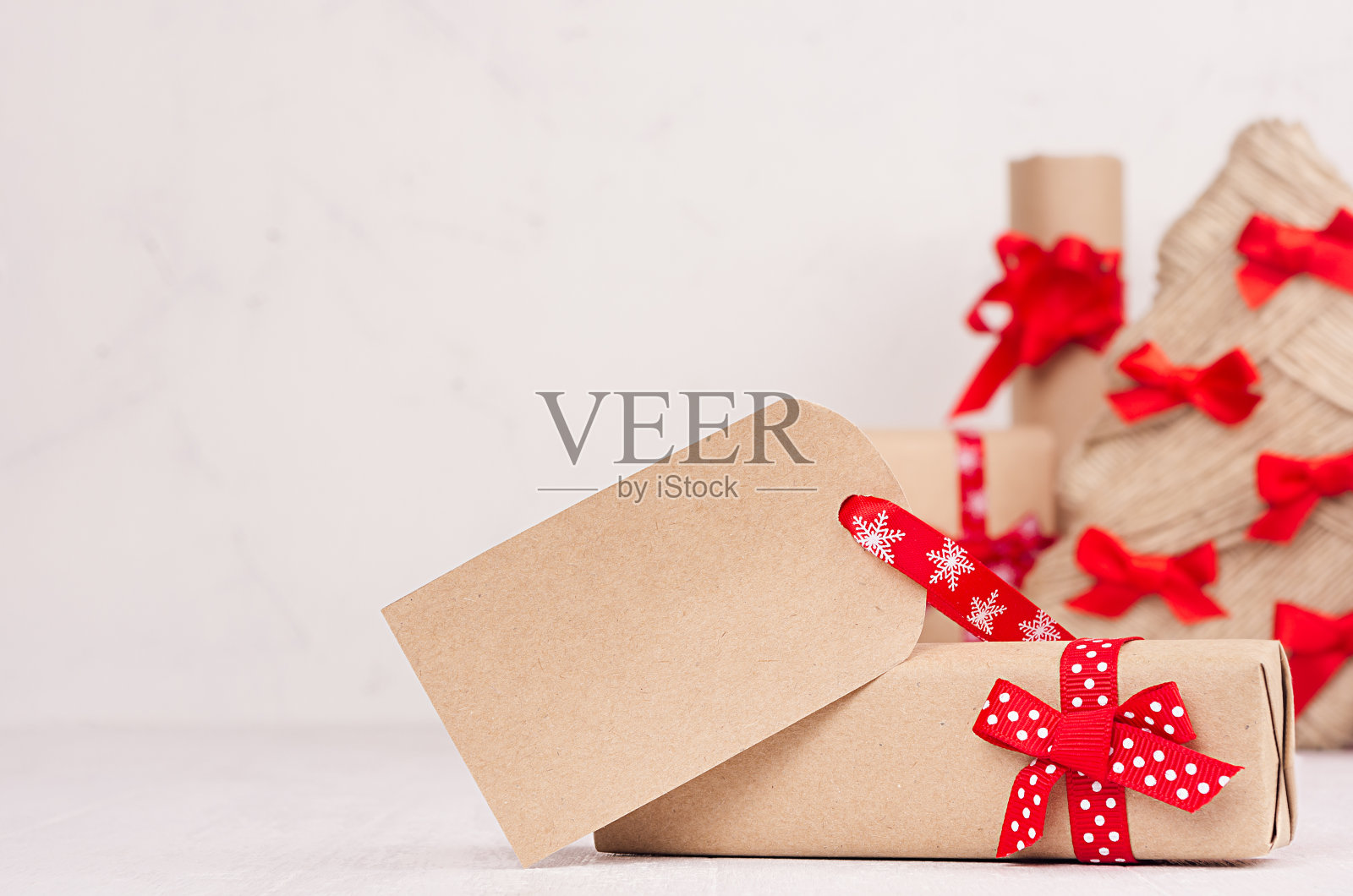 圣诞礼盒与空白问候标签和红色蝴蝶结和丝带特写在白色木板与复制空间。照片摄影图片