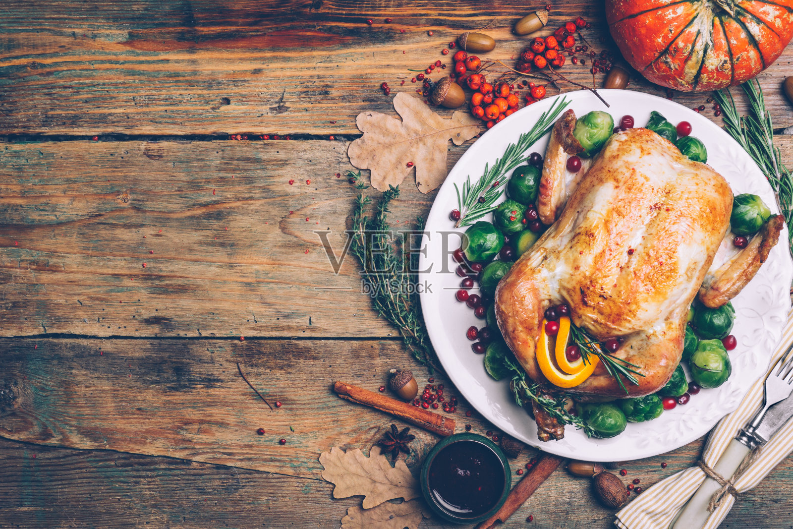 感恩节烤鸡,球芽甘蓝和香料放在质朴的木桌上。感恩节晚餐或秋天晚餐的概念背景与秋天的树叶。感恩节餐桌设置背景。照片摄影图片