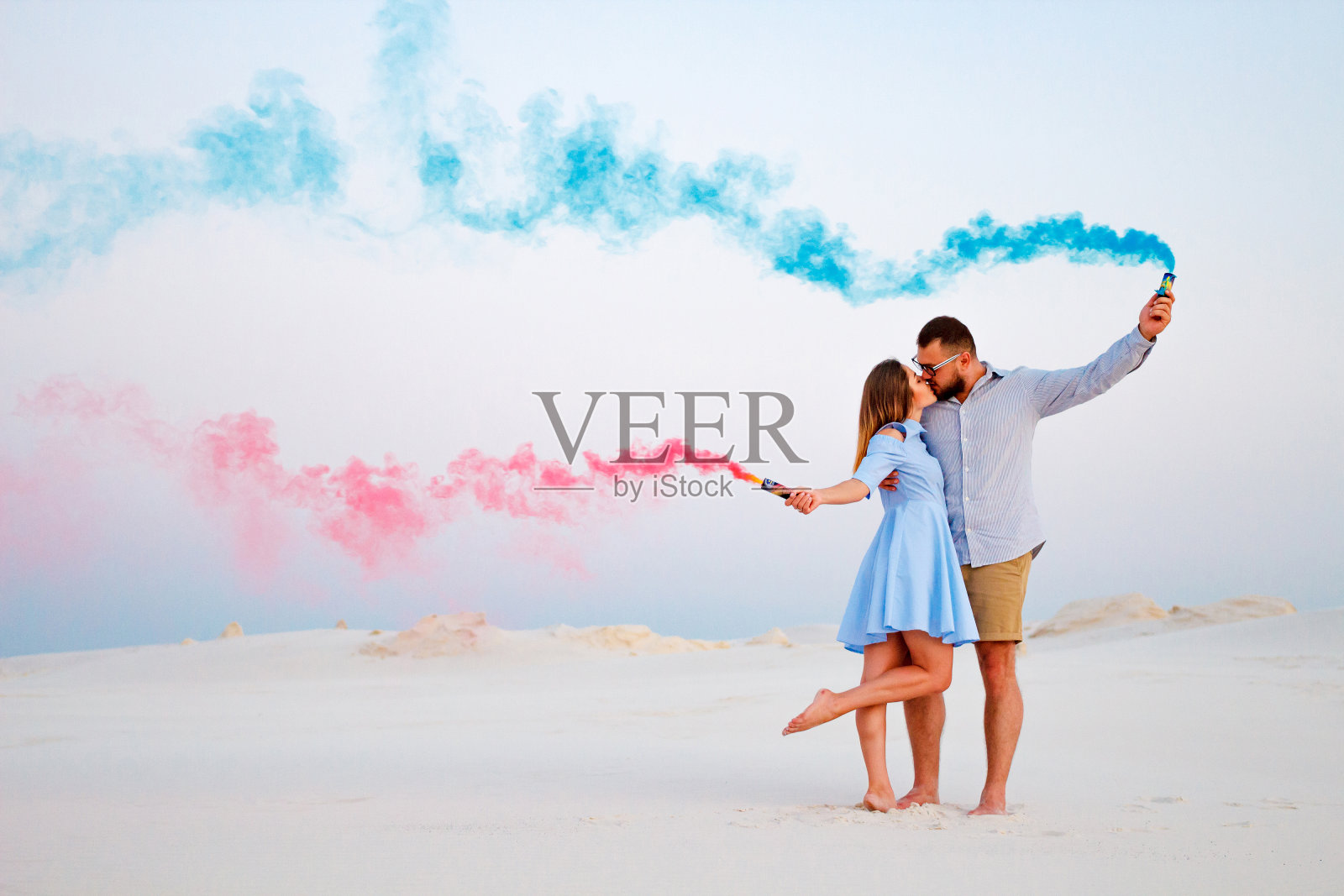 年轻的夫妇亲吻和手握彩色烟雾,浪漫的夫妇与蓝色和红色烟雾炸弹在海滩上照片摄影图片