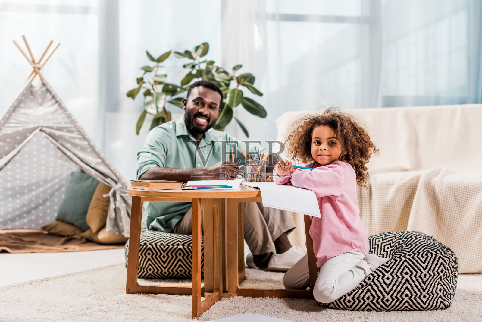 一位非裔美国父亲在客厅里帮助女儿画画,看着照相机照片摄影图片