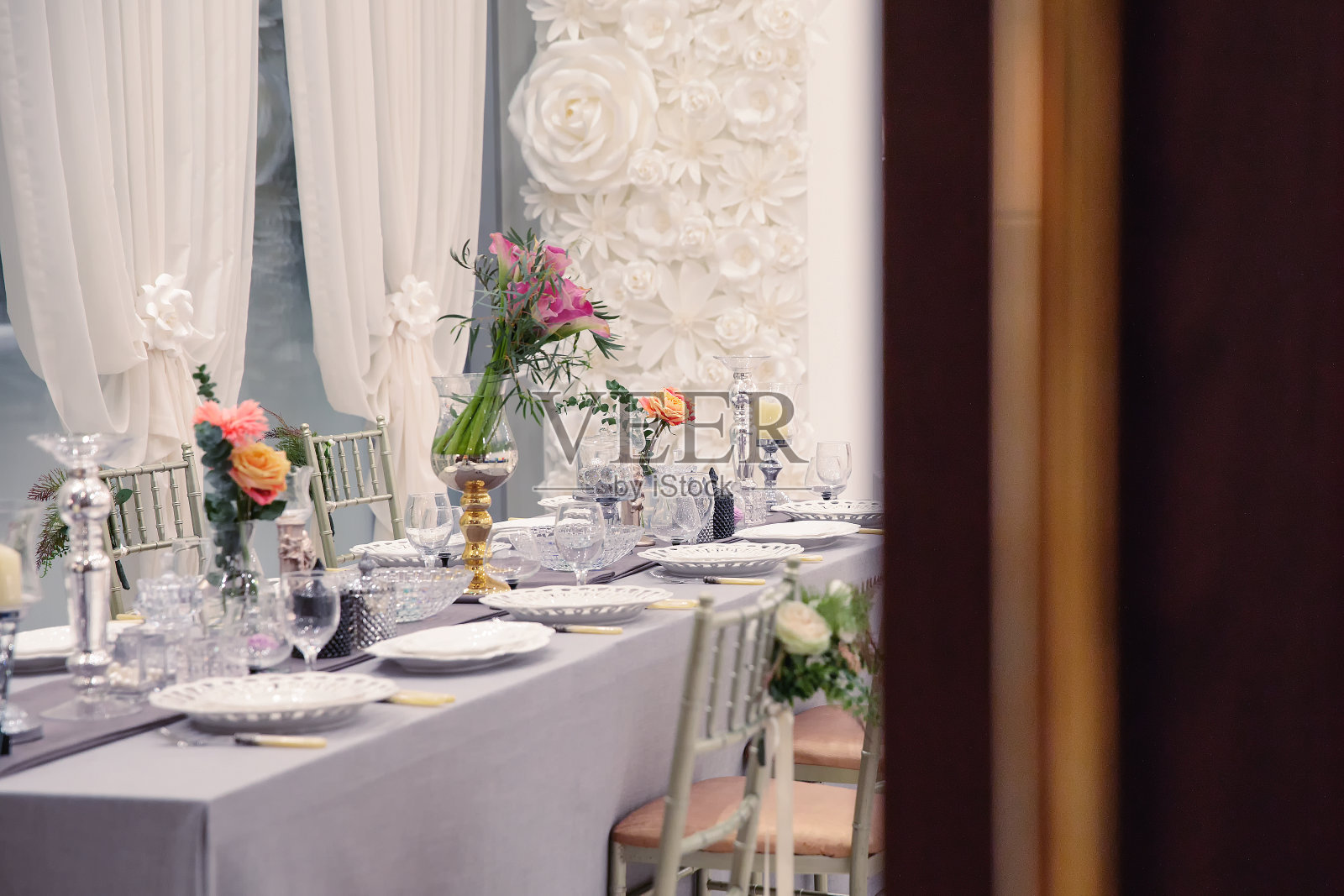 鲜花和玻璃器皿聚会室配有漂亮的餐桌-从门口望过去照片摄影图片