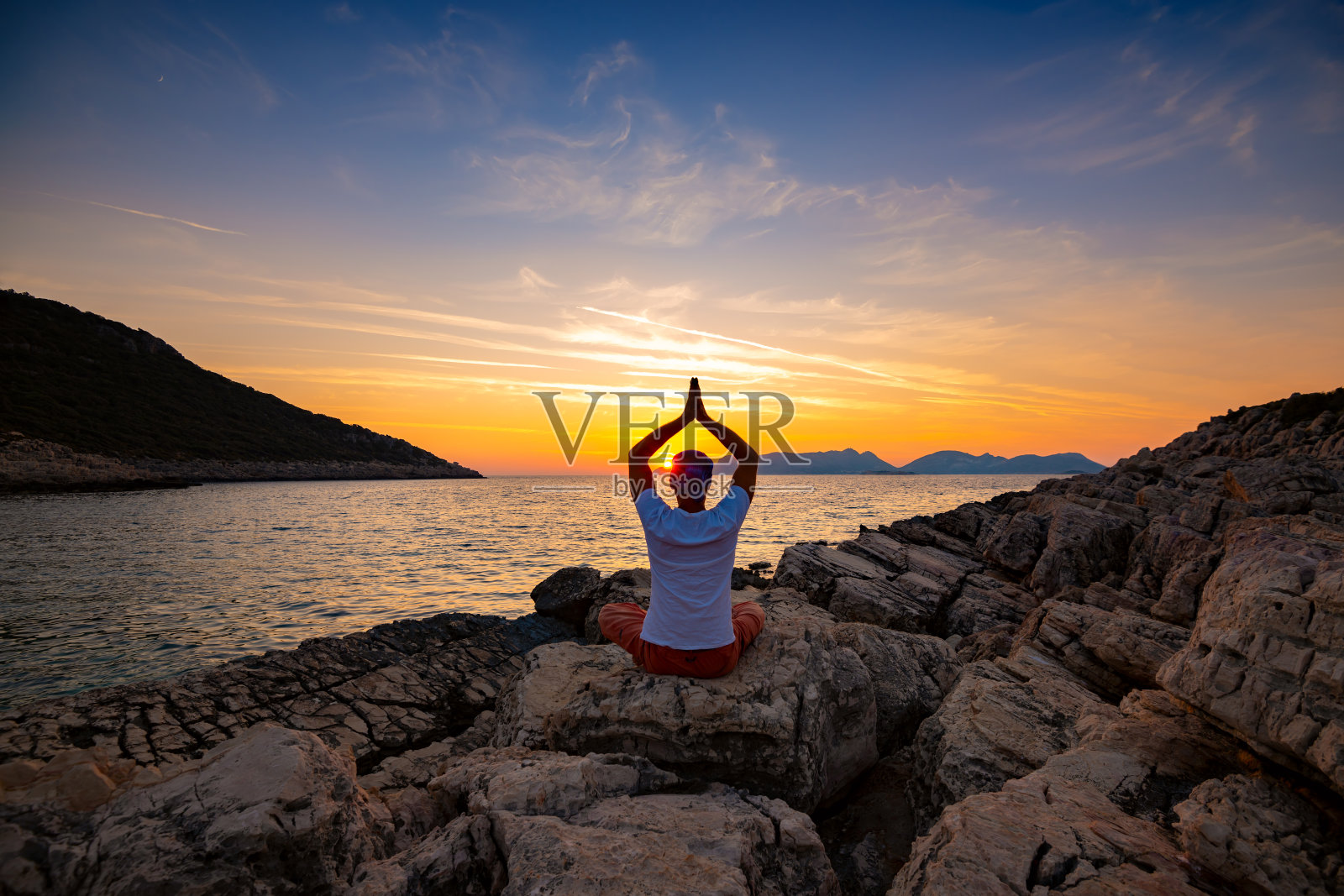 日落时分,游客坐在岩石海岸上练习瑜伽照片摄影图片