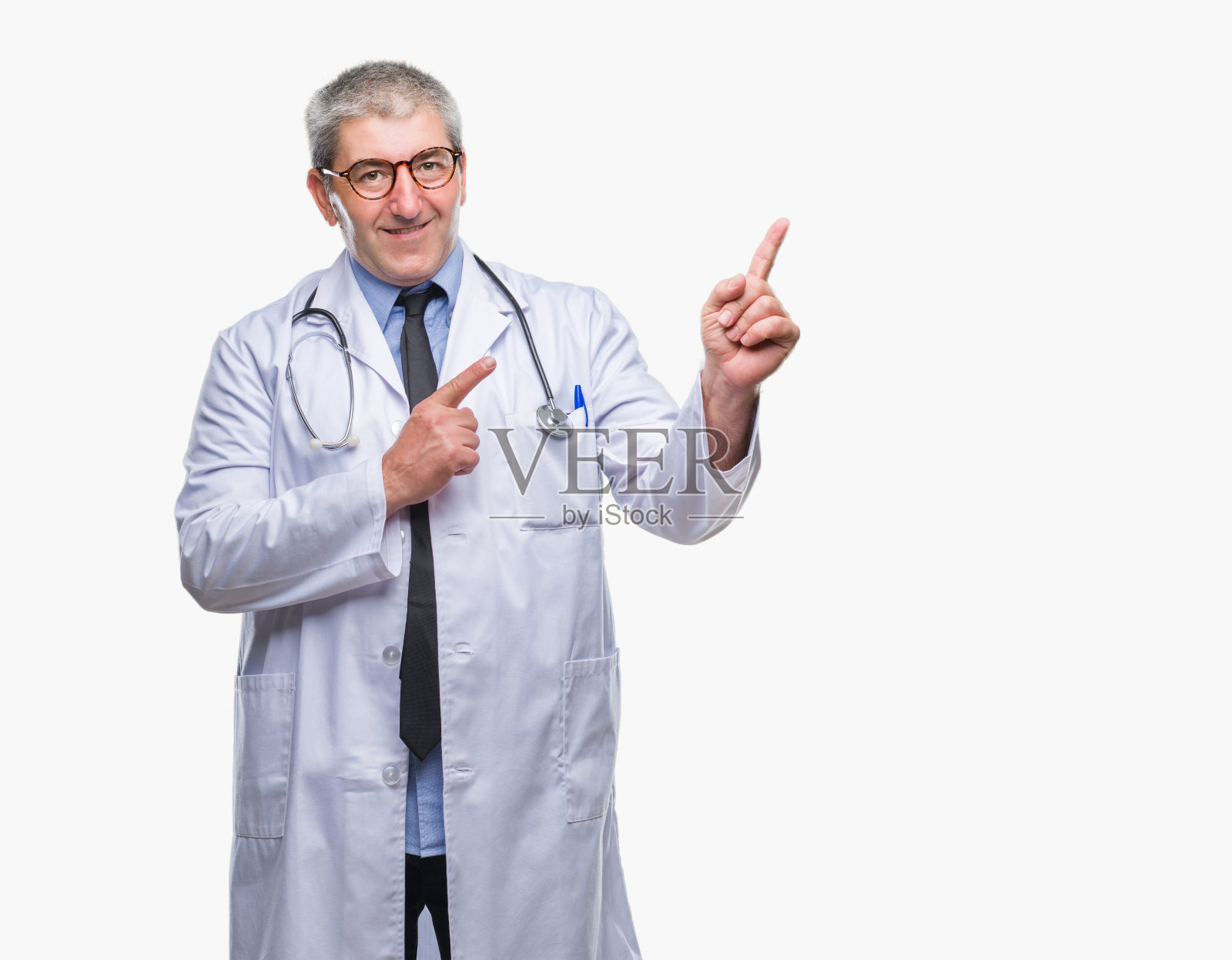 英俊的资深医生男子隔着孤立的背景微笑着看着镜头,双手和手指指向一边。照片摄影图片