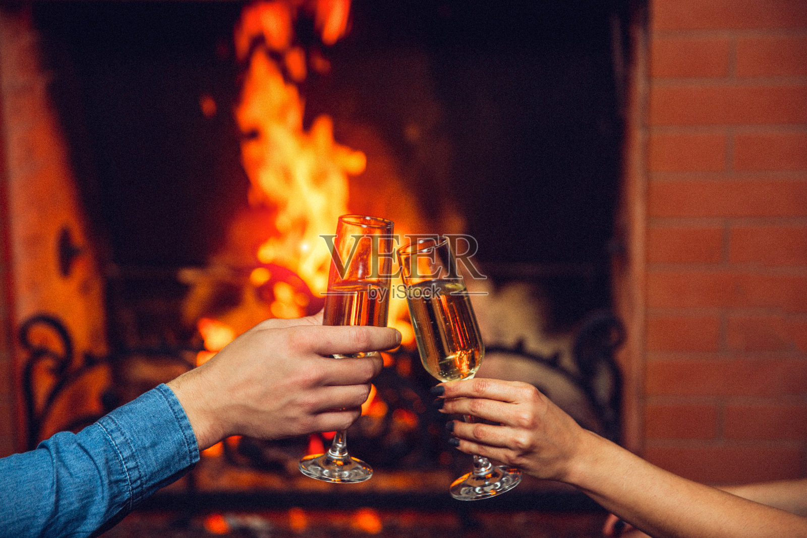 剪切的观点,男人和女人的手拿着酒杯与香槟。他们在壁炉前触摸它。照片摄影图片