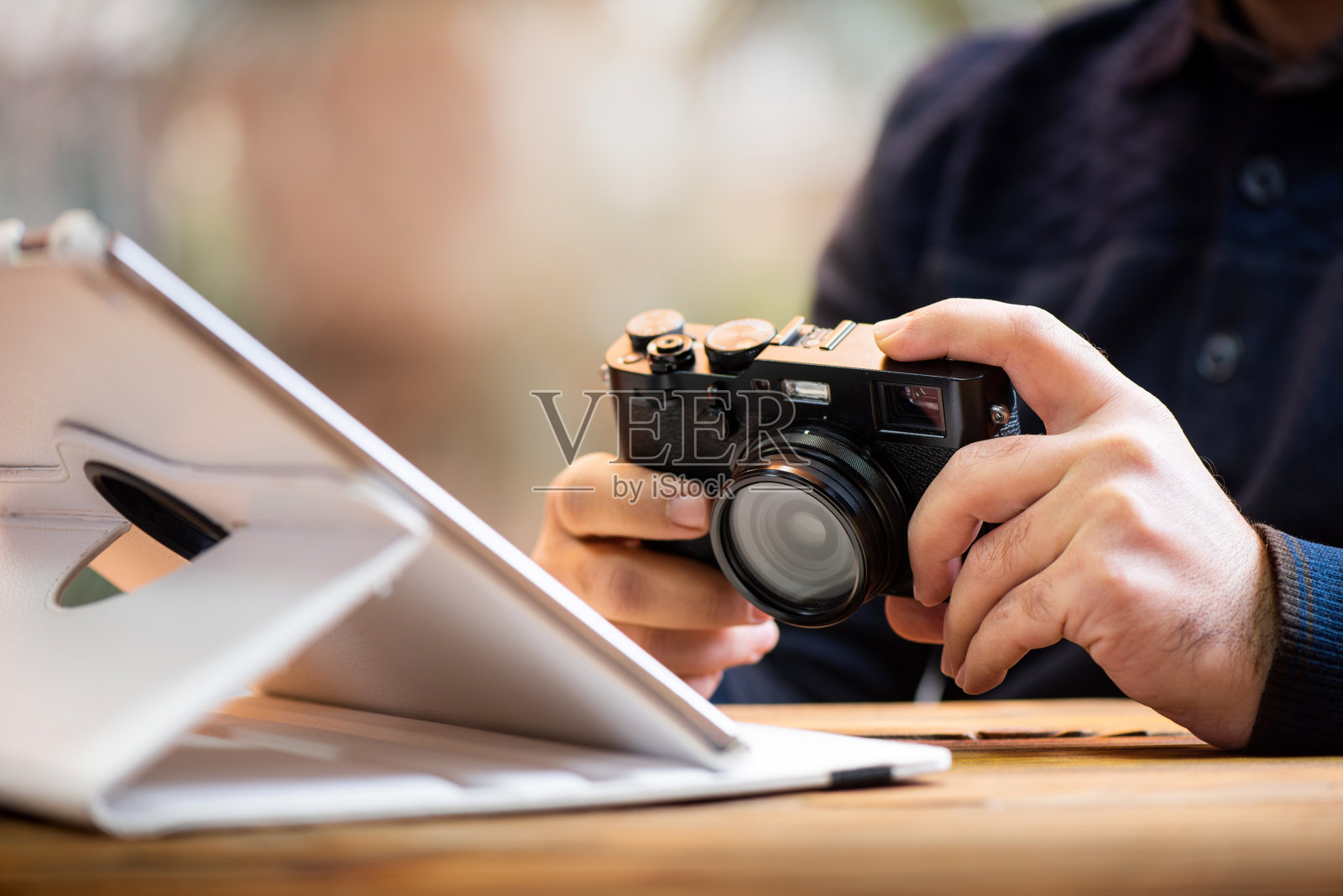 摄影师工作在平板电脑和持有他的数字测距相机照片摄影图片