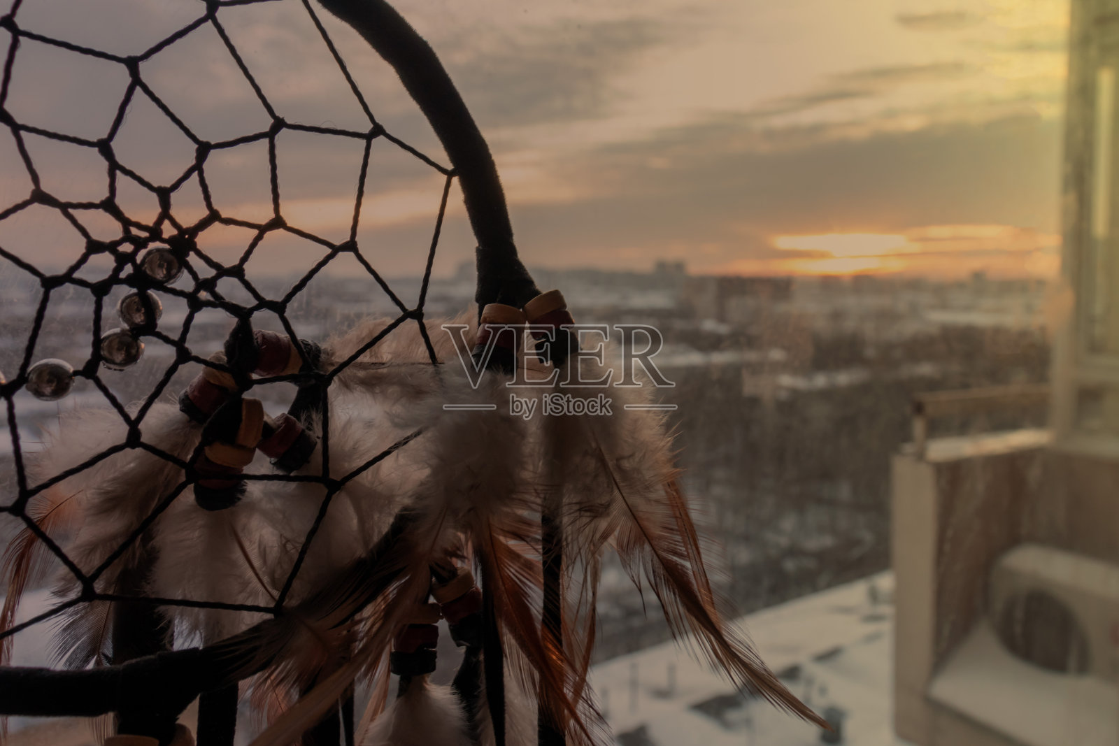 手工捕梦网挂在黄昏的百叶窗上。黑色剪影的传统魔术护身符,以保护梦和坏的灵魂照片摄影图片