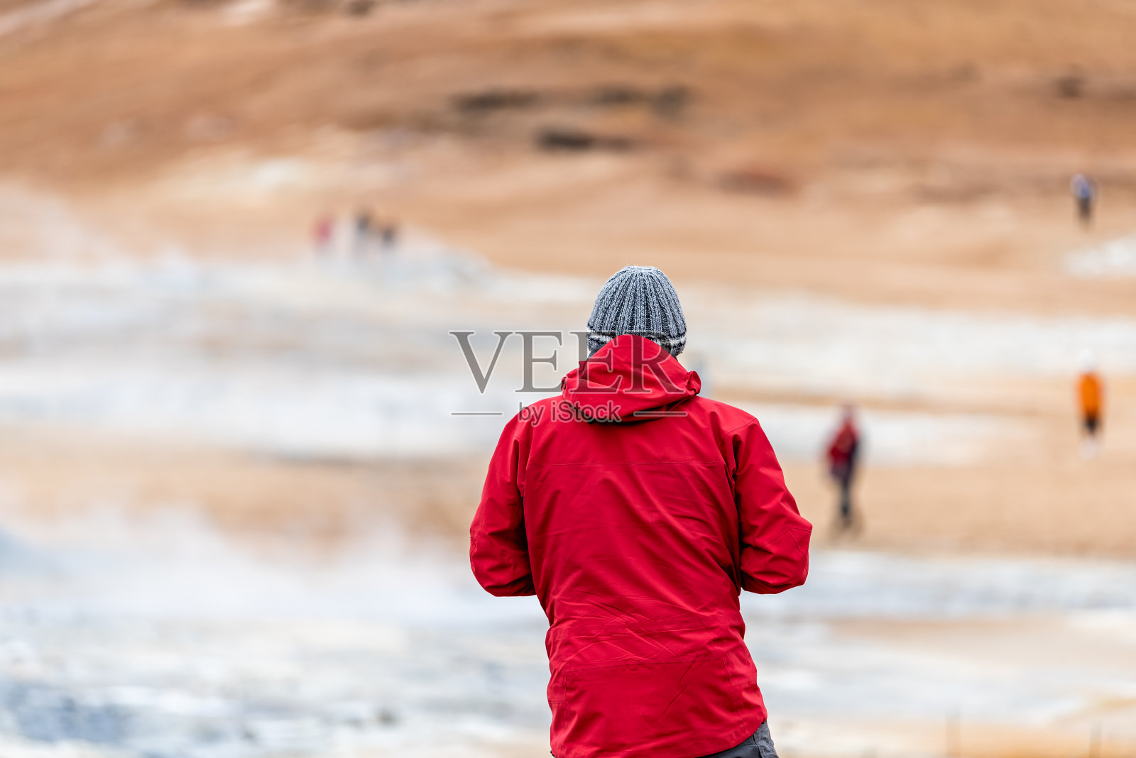 一名身穿红色夹克的男子背对着Myvatn湖地热景点附近的间歇泉看风景照片摄影图片