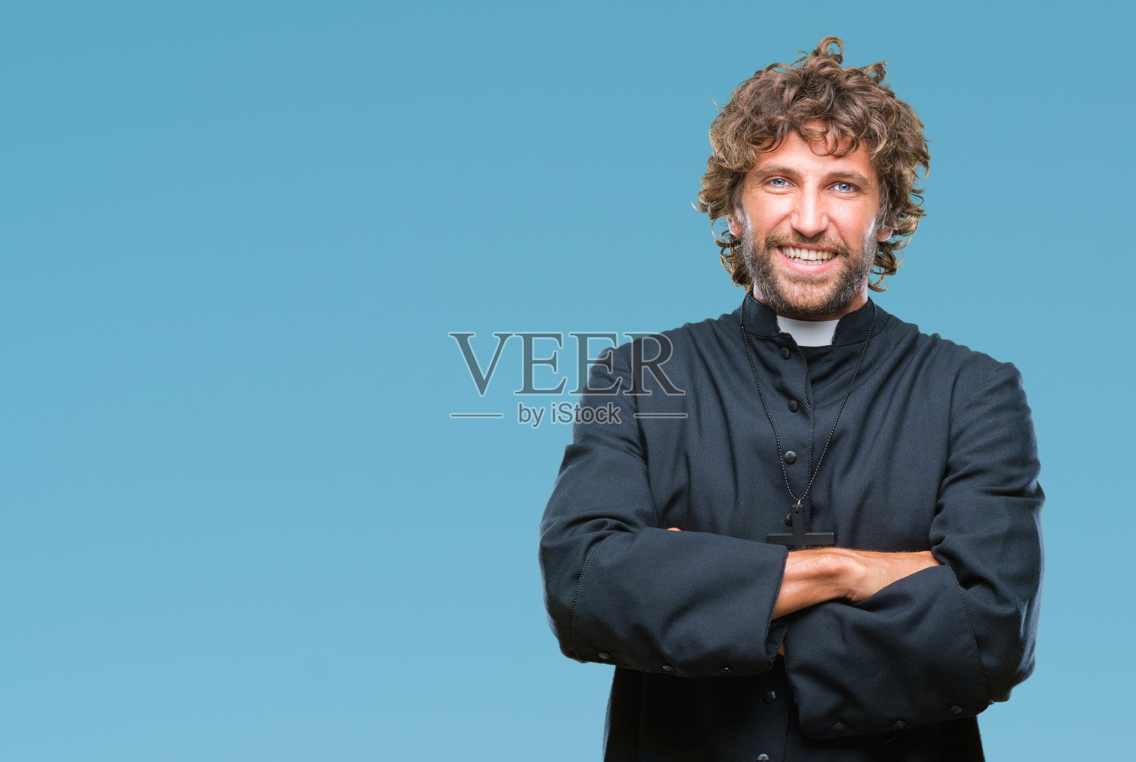 英俊的西班牙裔天主教神父在孤立的背景下,微笑着双臂交叉看着镜头。积极的人。照片摄影图片