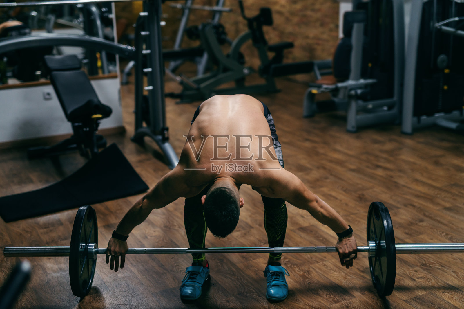 年轻强壮的白人赤膊健美运动员举杠铃。健身房室内。照片摄影图片