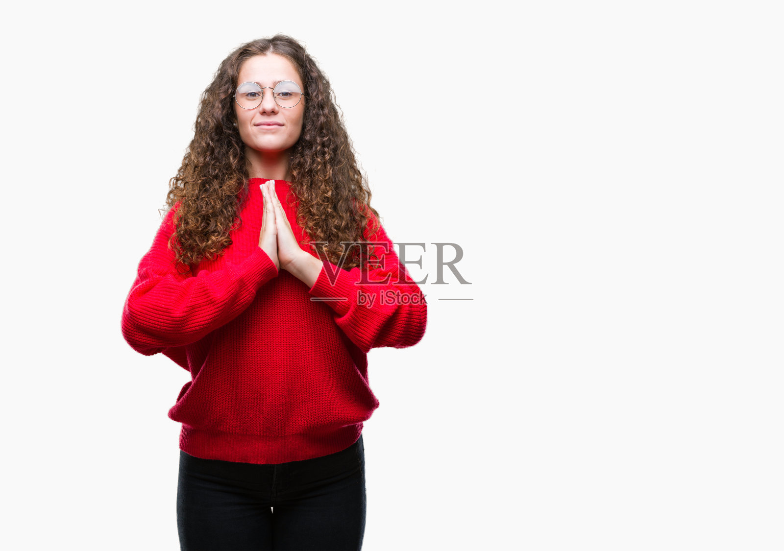 美丽的黑发卷曲的年轻女孩戴着眼镜和冬天的毛衣在孤立的背景祈祷与手一起请求宽恕微笑自信。照片摄影图片
