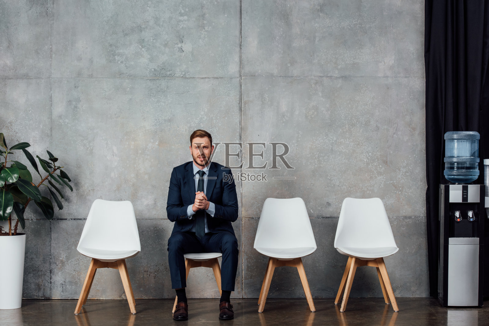 商人穿着西装,双手合十坐在候车厅里,看着镜头照片摄影图片