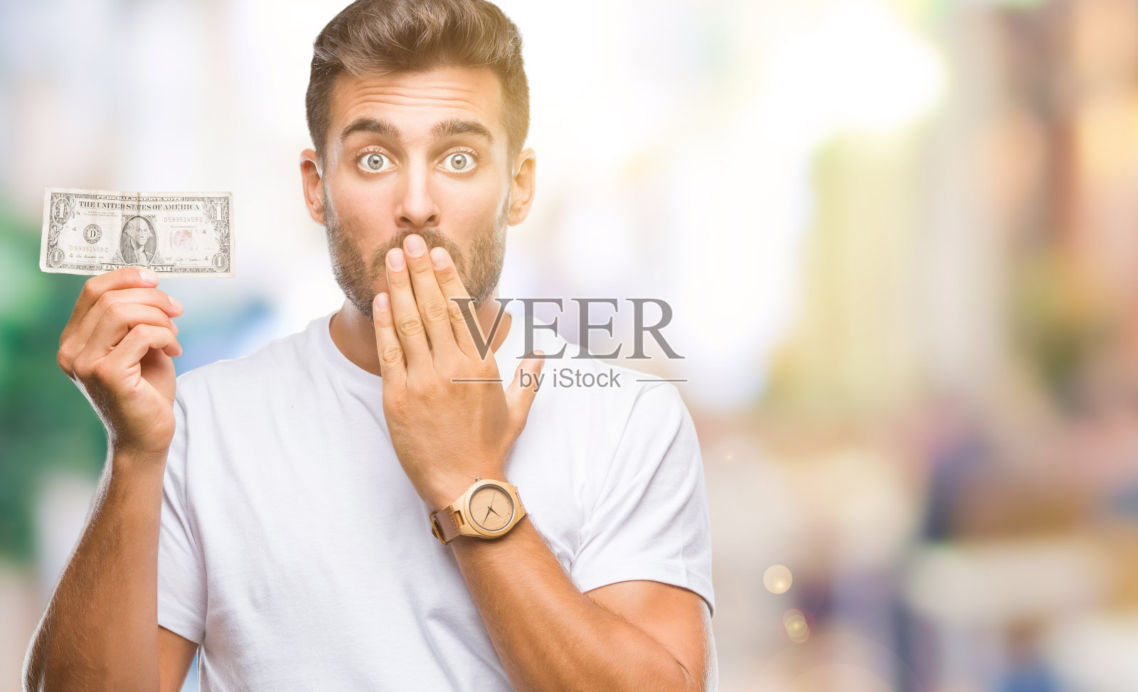 年轻英俊的男子抱着美元越过孤立的背景,用手捂着嘴,为错误而感到震惊,表情恐惧,在沉默中害怕,秘密的概念照片摄影图片