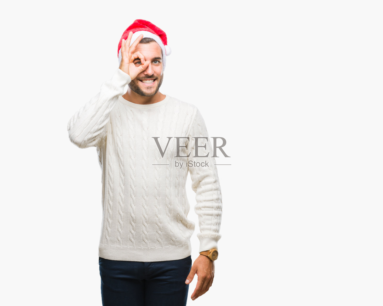 年轻英俊的男人戴着圣诞老人帽在孤立的背景做着ok手势与手微笑,眼睛透过手指看与快乐的脸。照片摄影图片