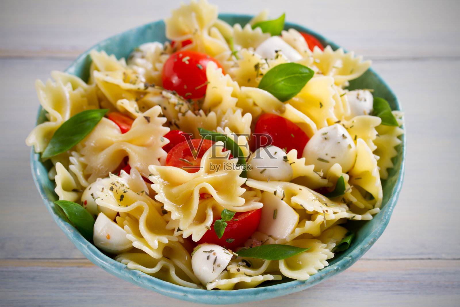 意大利番茄意大利面沙拉。木桌上的碗里有马苏里拉奶酪、番茄和罗勒照片摄影图片