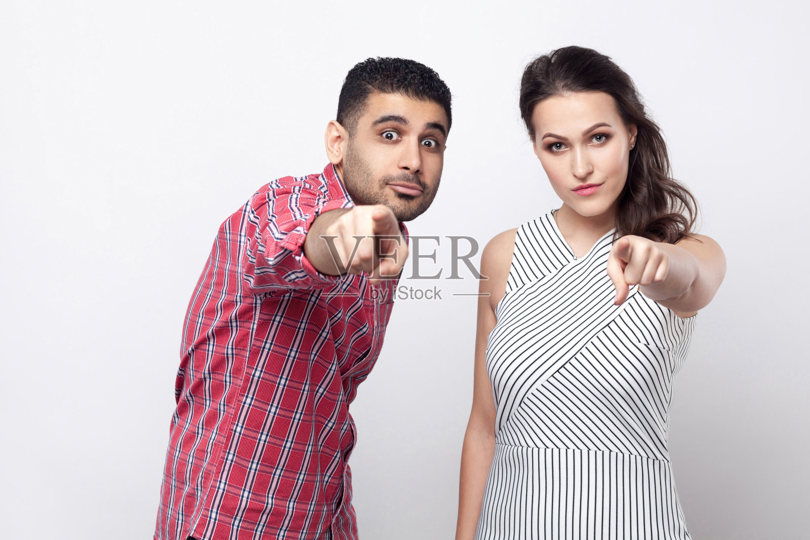 肖像严肃骄傲的英俊男子在红色格子衬衫和美丽的女人在白色条纹连衣裙站着,指向和看着相机。照片摄影图片