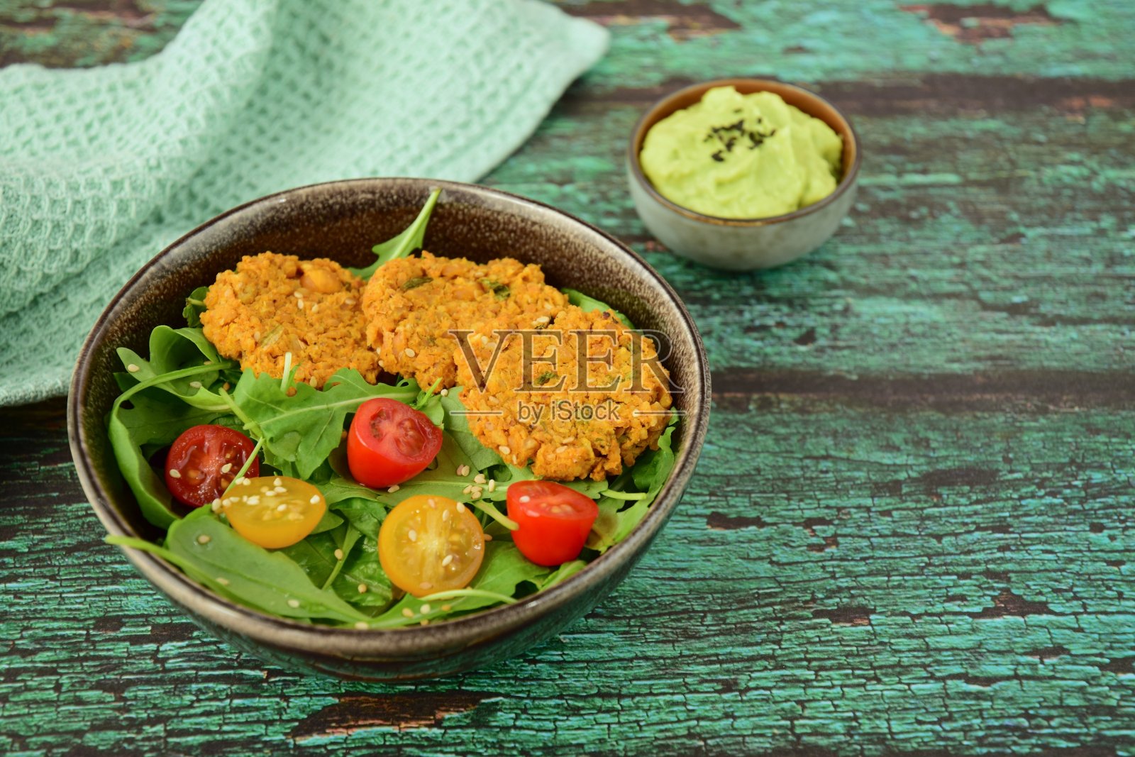 芝麻菜沙拉配圣女果,鹰嘴豆馅饼,鳄梨酱和芝麻。绿色背景照片摄影图片