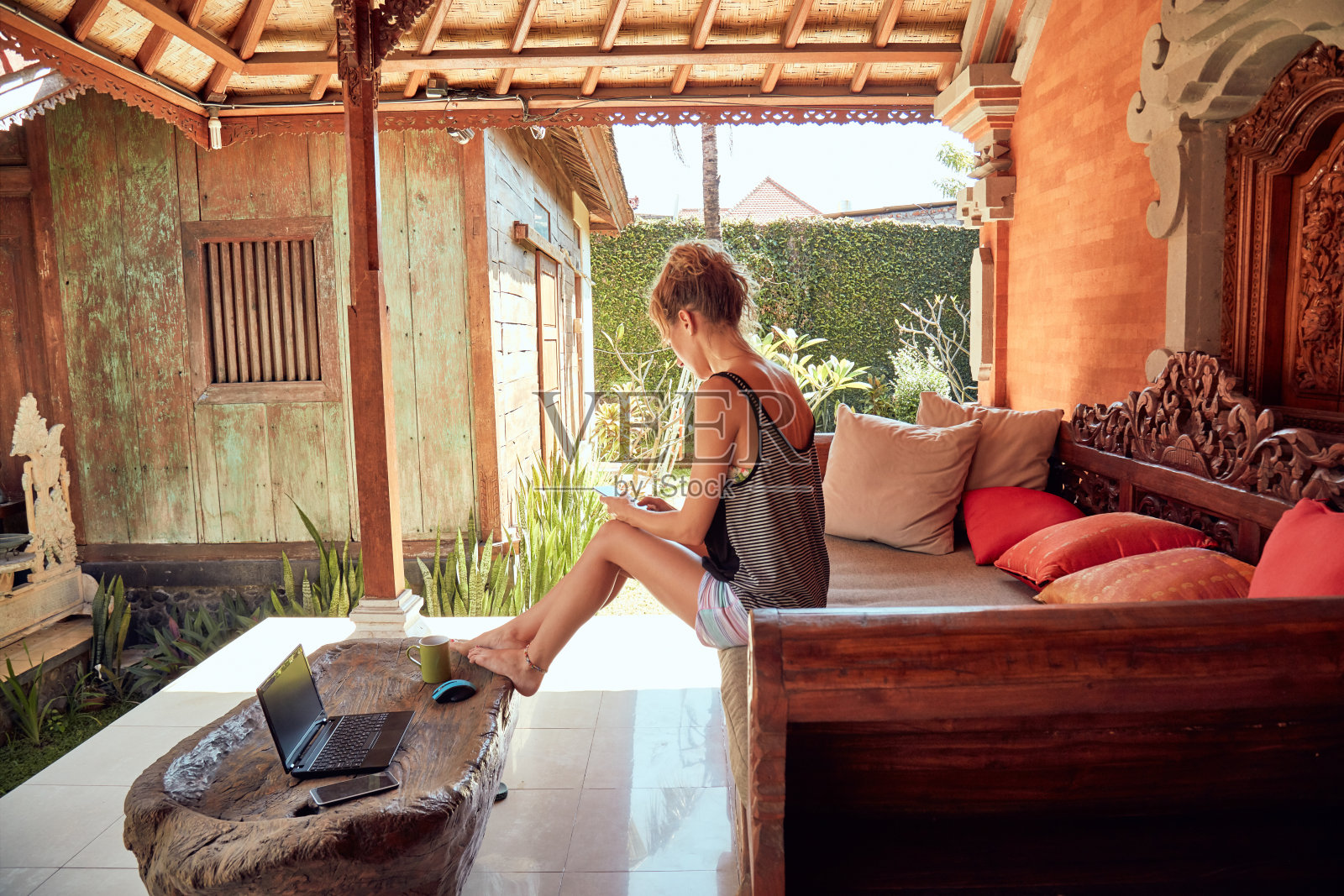 一个夏天在自家门廊上用笔记本电脑、手机喝咖啡的女人。照片摄影图片