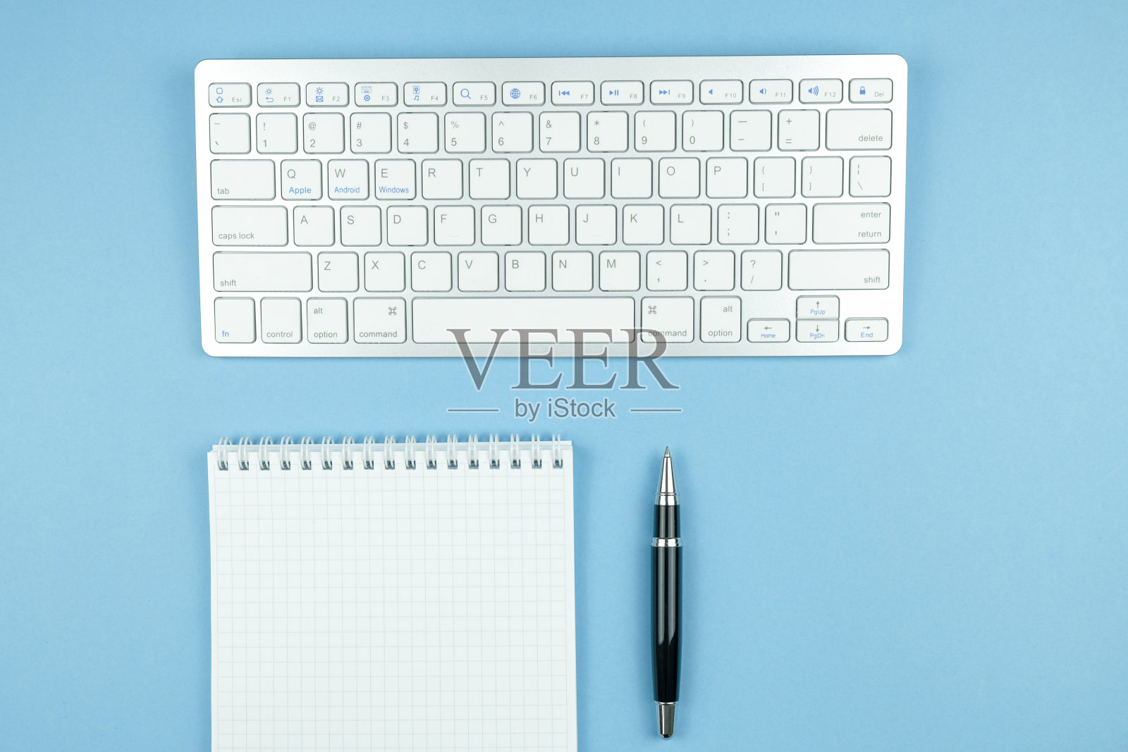 用白纸和笔检查笔记本,蓝色背景上的白色无线键盘。照片摄影图片