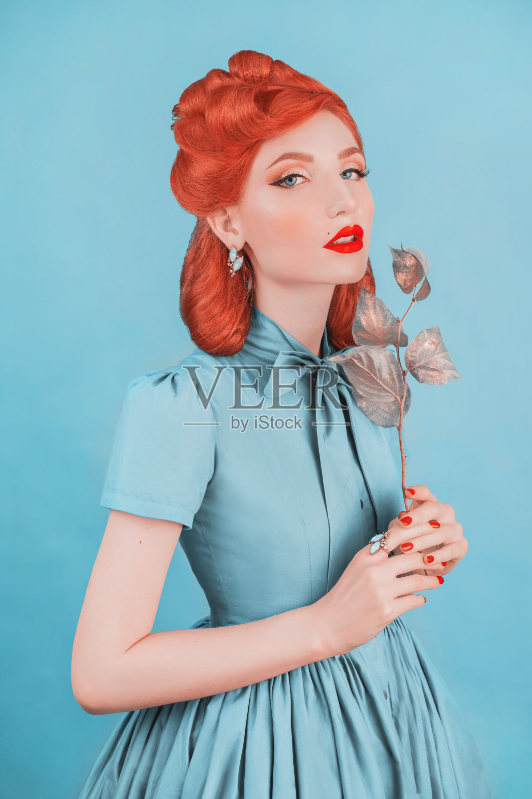 穿着蓝色复古裙的魅力女人。最小的颜色概念。红发模特与复古发型在柔和的蓝色背景。柔和的颜色。女士优雅。宏伟的穿。魅力简约风格照片摄影图片