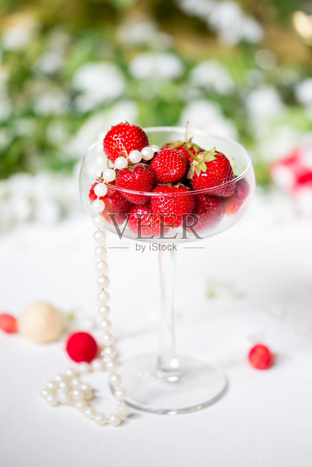 在一棵开花的苹果树的背景下,一个玻璃高脚杯中成熟的红色草莓。照片摄影图片