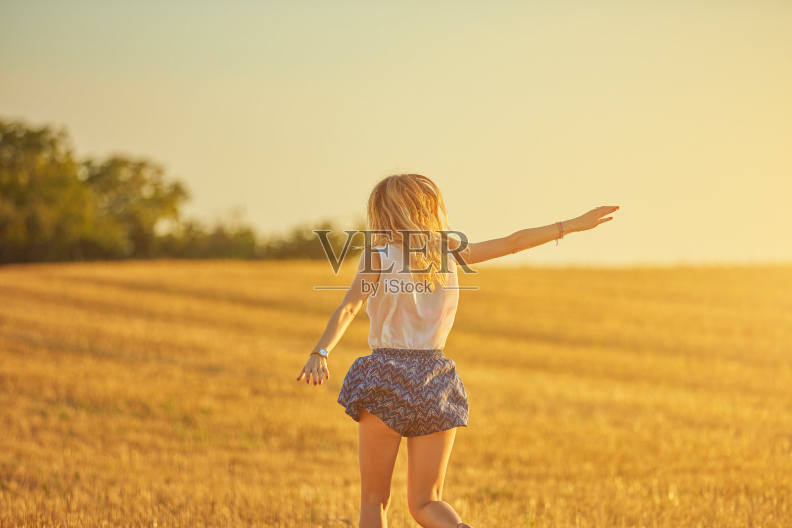 可爱的年轻女子在麦田里跳跃。照片摄影图片