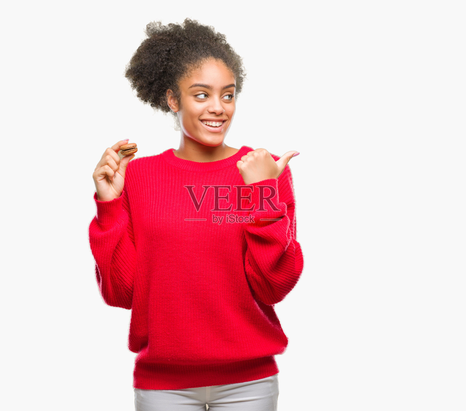 年轻的非洲裔美国妇女吃巧克力马卡龙在孤立的背景指向和显示与拇指向上的一边与快乐的脸微笑照片摄影图片