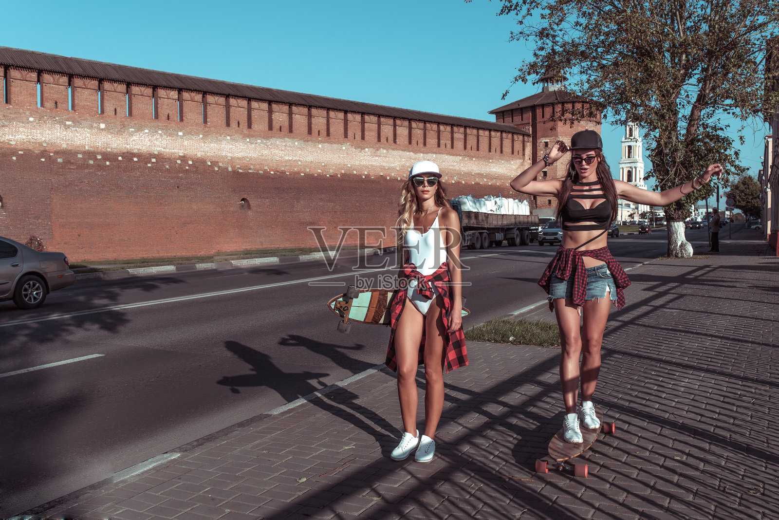 美丽的女孩女朋友在夏天的城市。步行,骑长板滑板。带着长头发和棒球帽玩得开心的微笑。文本的空闲空间。背景是有汽车的道路。照片摄影图片