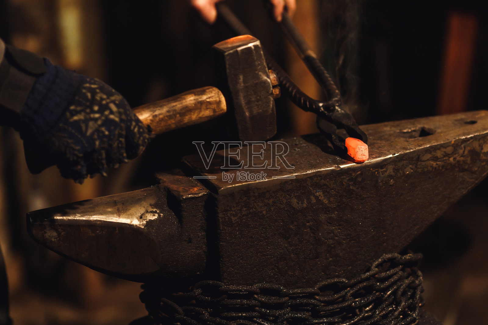 铁匠在铁匠铺的铁砧上手工锻造红热的金属。照片摄影图片